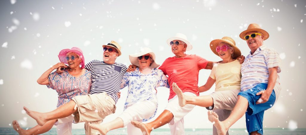 six elderly people at the beach wearing sunhats and sunglasses, kicking their feet up in a line