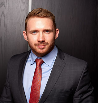 Photo of a bearded man in black suit, blue shirt and red tie smiling at the camera