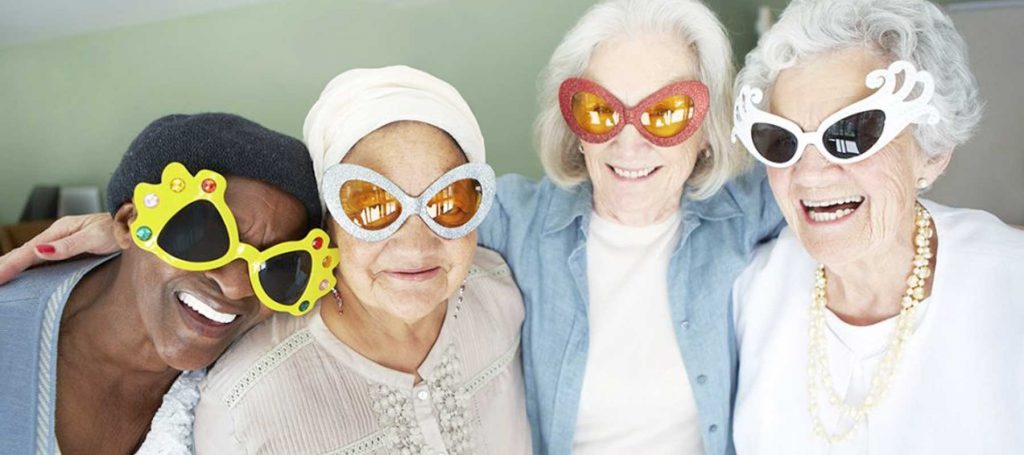 Four elderly woman in fun oversized glasses smiling in a nursing home