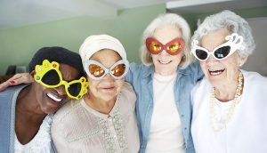 Four elderly woman in fun oversized glasses smiling at an aged care facility