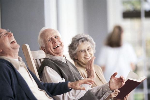 Three elderly people leaning back and laughing at a nursing home