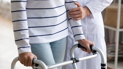 a person on crutches wearing a white shirt with black stripes has their arm held by a nurse in a white coat