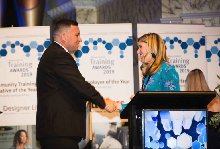 A man in a black suit shaking the hand of a smiling woman behind the podium at the Training Awards 2019